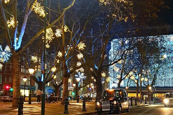 Trees strung with star-shaped lights along an avenue at dusk, a black cab passing