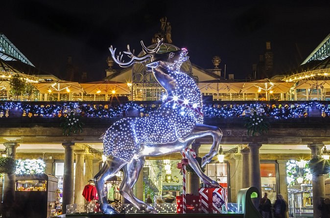 A reindeer sculpture of silver lights standing in front of a lit market hall