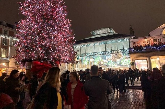 A tall tree lit pink in a crowded piazza beside a glass-roofed market